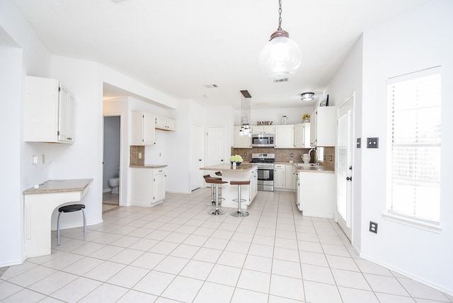 kitchen with a wealth of natural light, appliances with stainless steel finishes, a kitchen bar, and white cabinetry