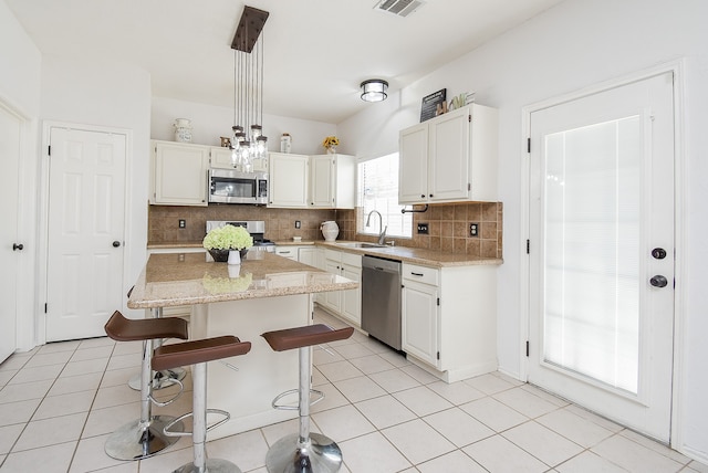 kitchen featuring a kitchen island, stainless steel appliances, sink, light stone countertops, and tasteful backsplash