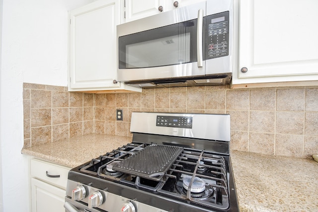 kitchen featuring white cabinets, stainless steel appliances, light stone counters, and backsplash