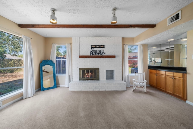 unfurnished living room with beamed ceiling, a wealth of natural light, carpet flooring, and a textured ceiling