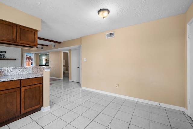 kitchen featuring light tile patterned flooring, beam ceiling, a textured ceiling, backsplash, and light stone countertops