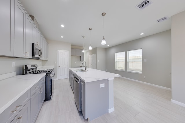 kitchen with a kitchen island with sink, gray cabinetry, sink, pendant lighting, and appliances with stainless steel finishes