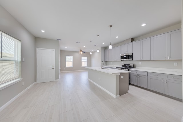 kitchen with pendant lighting, sink, gray cabinetry, a kitchen island with sink, and stainless steel appliances