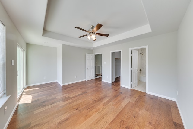 unfurnished bedroom featuring light hardwood / wood-style flooring, a tray ceiling, a walk in closet, and connected bathroom