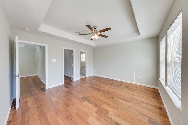 unfurnished bedroom featuring ceiling fan, a tray ceiling, light hardwood / wood-style floors, and a walk in closet