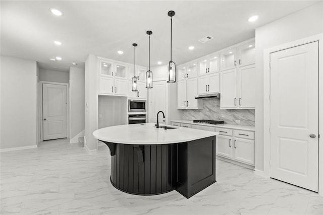 kitchen with tasteful backsplash, appliances with stainless steel finishes, sink, an island with sink, and white cabinetry