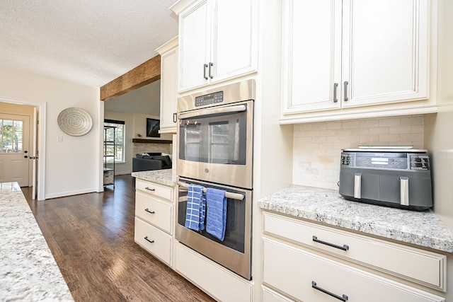 kitchen featuring backsplash, light stone counters, a textured ceiling, stainless steel double oven, and dark wood-type flooring