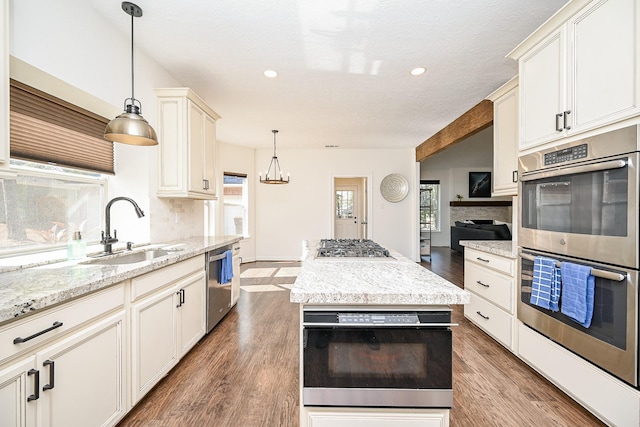 kitchen with pendant lighting, dark wood-type flooring, sink, light stone counters, and stainless steel appliances