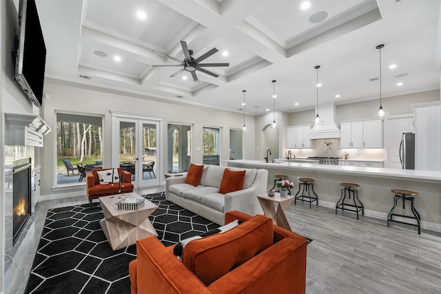 living room with ceiling fan, beam ceiling, french doors, coffered ceiling, and light wood-type flooring