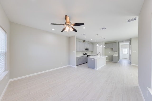 kitchen with an island with sink, sink, hanging light fixtures, appliances with stainless steel finishes, and gray cabinets