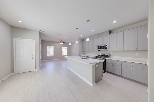 kitchen with ceiling fan, gray cabinetry, decorative light fixtures, a center island with sink, and appliances with stainless steel finishes