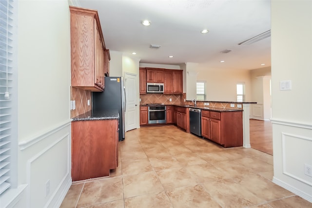 kitchen featuring kitchen peninsula, backsplash, appliances with stainless steel finishes, dark stone countertops, and sink