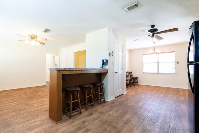 kitchen featuring hardwood / wood-style floors, black refrigerator, ceiling fan with notable chandelier, and a breakfast bar area