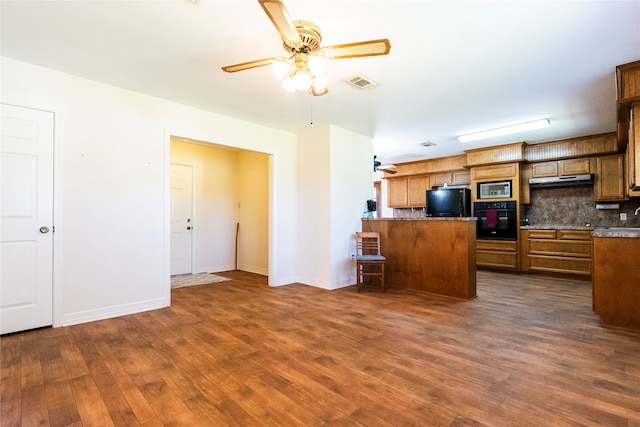 kitchen featuring a kitchen breakfast bar, dark wood-type flooring, kitchen peninsula, backsplash, and black appliances