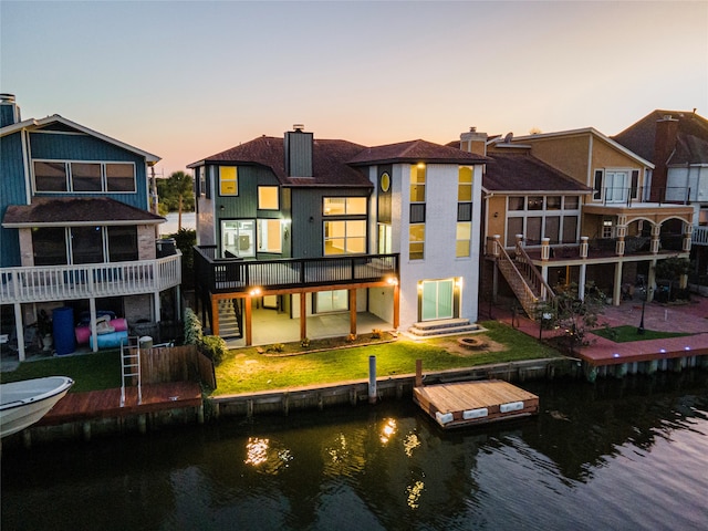 back house at dusk with a deck with water view and a lawn