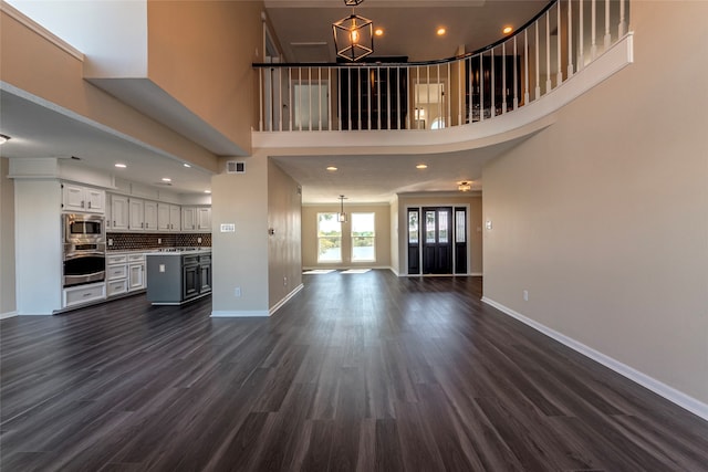 unfurnished living room featuring a towering ceiling, french doors, a chandelier, and dark hardwood / wood-style flooring