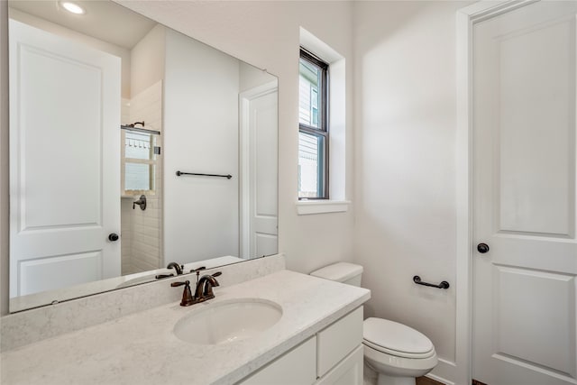 bathroom with a tile shower, vanity, and toilet