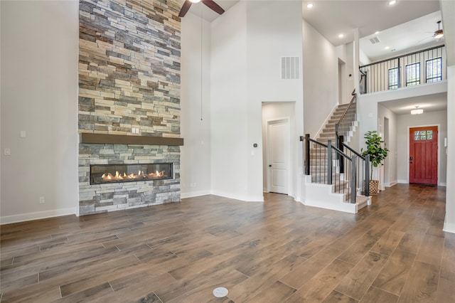 unfurnished living room with ceiling fan, dark wood-type flooring, a towering ceiling, and a stone fireplace