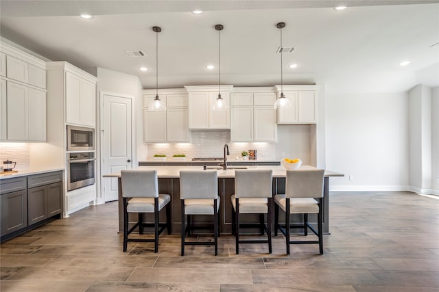 kitchen featuring decorative light fixtures, a center island with sink, stainless steel appliances, and a kitchen bar