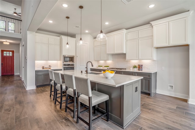 kitchen with an island with sink, gray cabinetry, hardwood / wood-style flooring, appliances with stainless steel finishes, and a breakfast bar