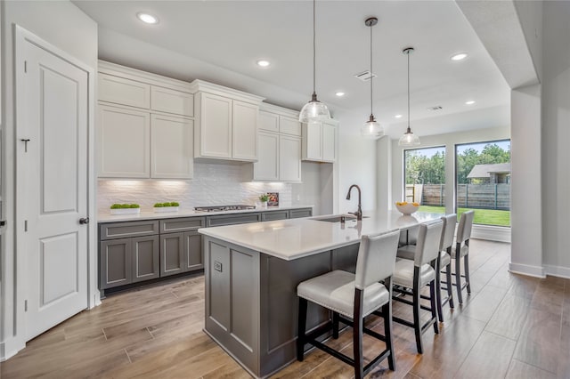 kitchen with light hardwood / wood-style floors, a breakfast bar, decorative light fixtures, sink, and an island with sink