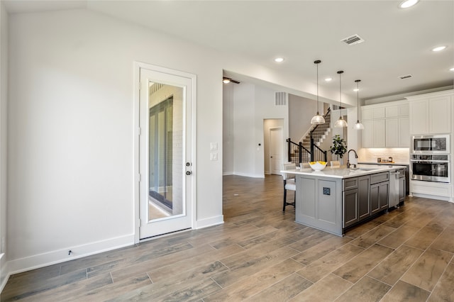 kitchen featuring hanging light fixtures, a center island with sink, hardwood / wood-style flooring, stainless steel appliances, and a breakfast bar area