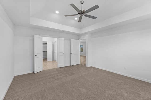 unfurnished bedroom with ceiling fan, a spacious closet, a raised ceiling, light colored carpet, and a closet