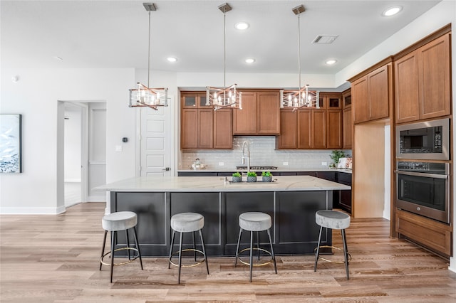 kitchen featuring appliances with stainless steel finishes, light stone countertops, a center island with sink, and light hardwood / wood-style flooring