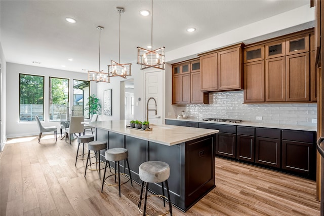 kitchen featuring a kitchen island with sink, light wood-type flooring, a kitchen breakfast bar, light stone counters, and hanging light fixtures