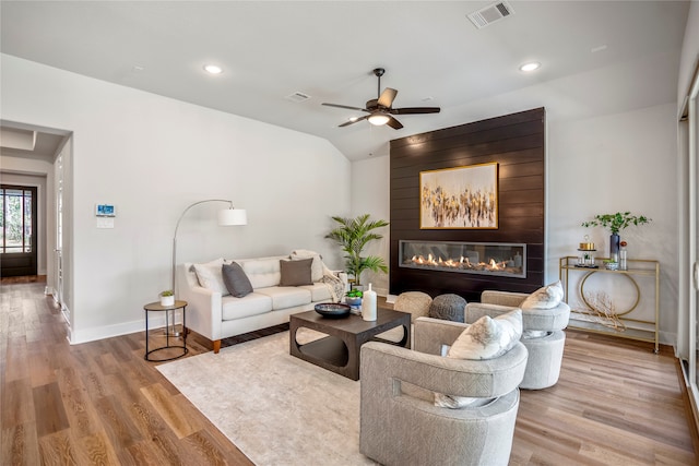 living room featuring ceiling fan, a large fireplace, and light hardwood / wood-style flooring