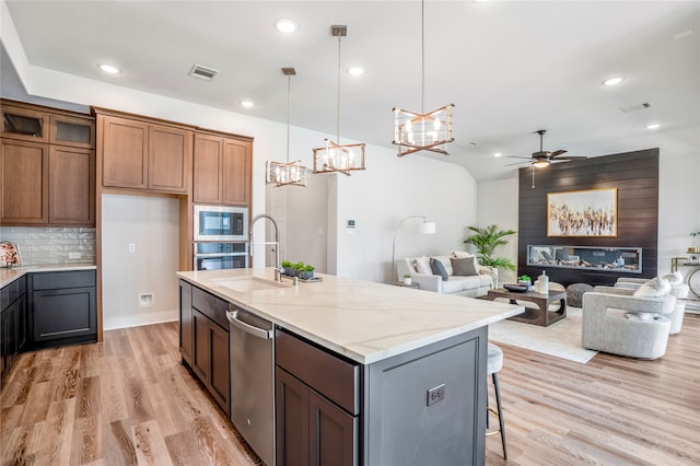 kitchen featuring an island with sink, decorative light fixtures, backsplash, light stone countertops, and light hardwood / wood-style floors