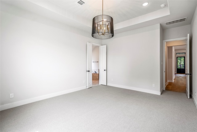 unfurnished room featuring a tray ceiling, carpet flooring, and an inviting chandelier