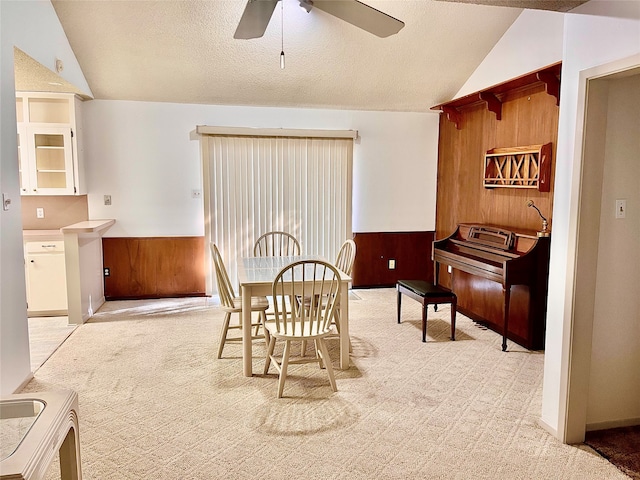 carpeted dining space featuring a textured ceiling, vaulted ceiling, wooden walls, and ceiling fan