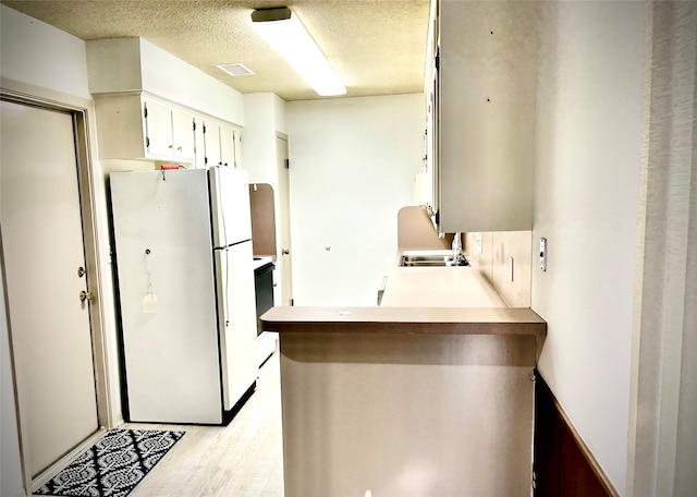 kitchen with white refrigerator, kitchen peninsula, sink, a textured ceiling, and light hardwood / wood-style floors