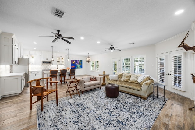 living room with ceiling fan with notable chandelier, light wood-type flooring, french doors, and a textured ceiling