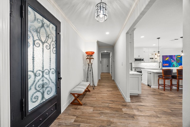 entrance foyer with ornamental molding, hardwood / wood-style floors, a chandelier, and sink