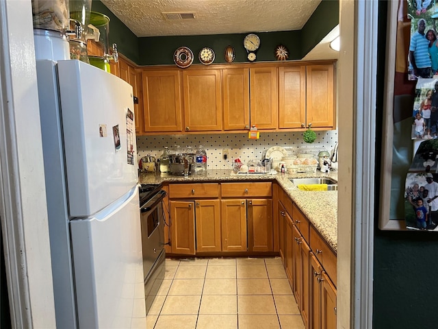 kitchen featuring black range with electric stovetop, sink, light stone counters, white fridge, and a textured ceiling