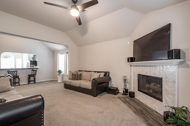 carpeted living room featuring a tiled fireplace, vaulted ceiling, and ceiling fan