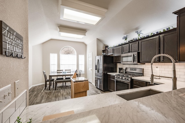 kitchen featuring vaulted ceiling, tasteful backsplash, dark brown cabinetry, stainless steel appliances, and light stone countertops