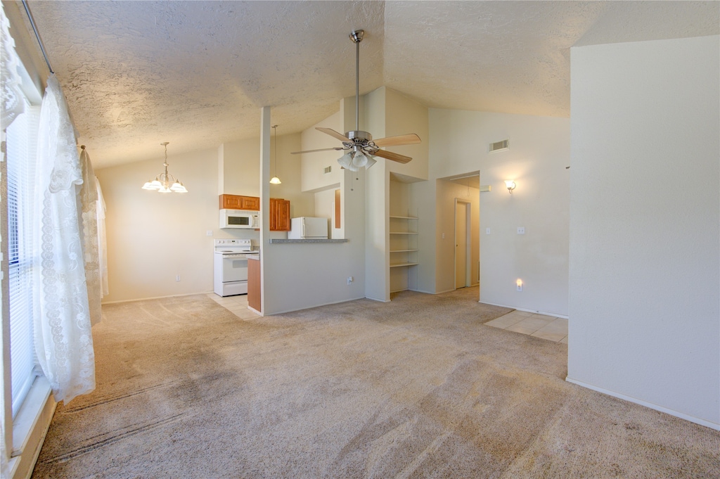 unfurnished living room featuring a textured ceiling, high vaulted ceiling, light colored carpet, ceiling fan with notable chandelier, and a healthy amount of sunlight