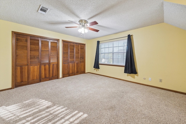 unfurnished bedroom featuring ceiling fan, lofted ceiling, a textured ceiling, two closets, and carpet floors