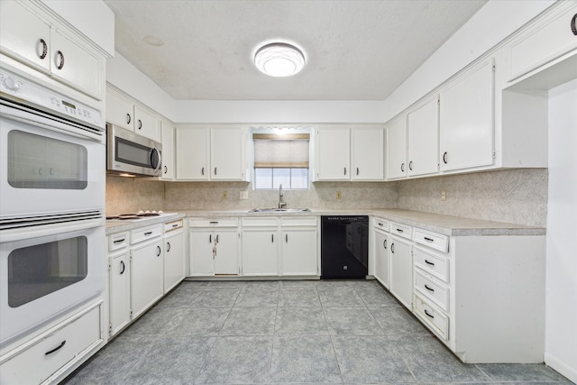 kitchen featuring sink, white double oven, dishwasher, light tile patterned floors, and white cabinetry