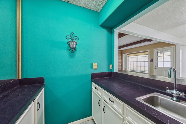 kitchen with a textured ceiling, sink, and white cabinetry