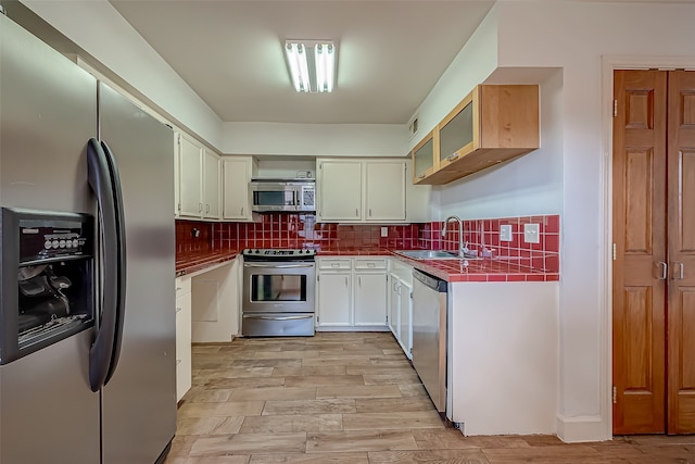 kitchen featuring decorative backsplash, appliances with stainless steel finishes, white cabinetry, light hardwood / wood-style floors, and sink