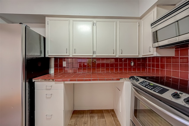 kitchen with tile counters, white cabinets, stainless steel appliances, and light hardwood / wood-style floors