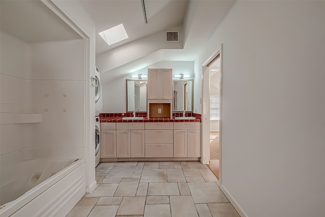 bathroom featuring vanity, tile patterned flooring, a bathtub, lofted ceiling with skylight, and stacked washer and clothes dryer