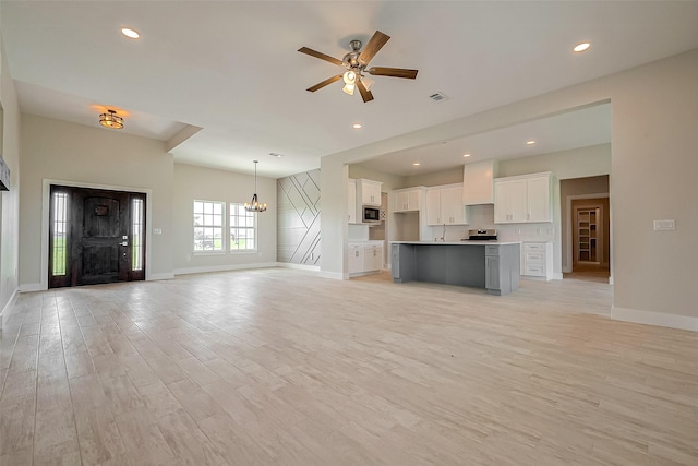 unfurnished living room featuring ceiling fan with notable chandelier and light wood-type flooring