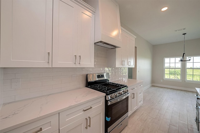 kitchen featuring gas range, light stone counters, premium range hood, white cabinets, and light wood-type flooring