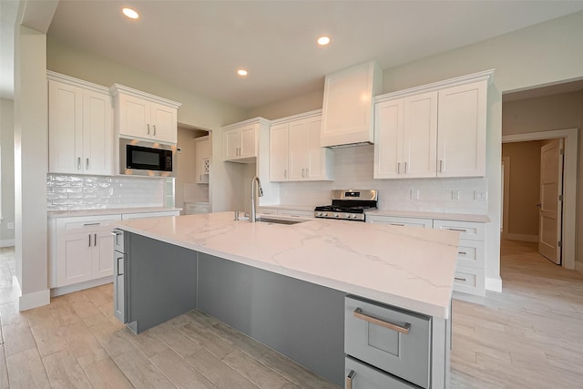 kitchen featuring white cabinetry, sink, stainless steel appliances, tasteful backsplash, and a center island with sink