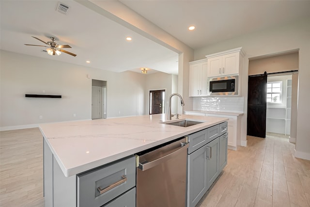 kitchen featuring appliances with stainless steel finishes, sink, a barn door, a center island with sink, and white cabinetry